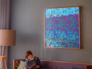 We Are One is an abstract landscape artwork featuring the ocean and trees in blues and some pinks placed on topic of a large sofa in a room.